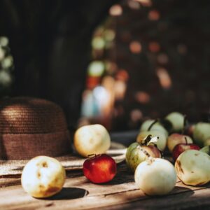 A collection of fresh apples on a wooden table with a hat, evoking a rustic, natural setting.